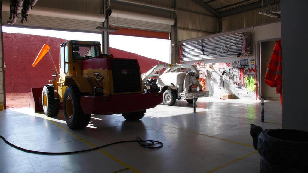 A wheel loader parked inside a workshop bay with the roller doors open