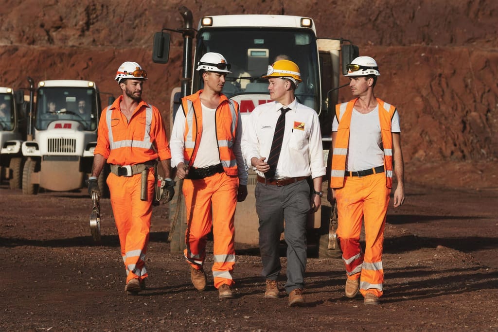Four crew members in high vis walking together past parked machinery