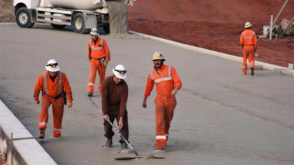 A crew screeding a large concrete pad with an agitator truck parked behind