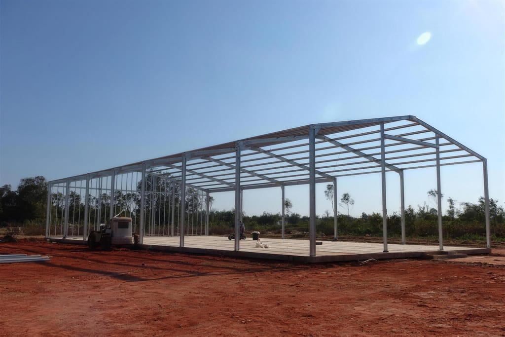 A bare steel portal frame standing on a new concrete slab, red dirt around it