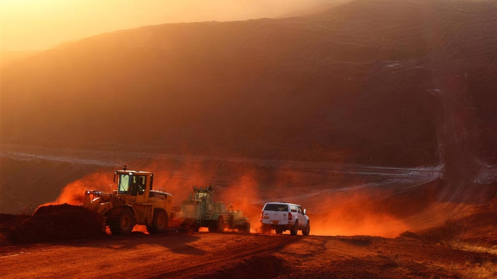 A wheel loader and a ute working a haul road at sunset, red dust in the air