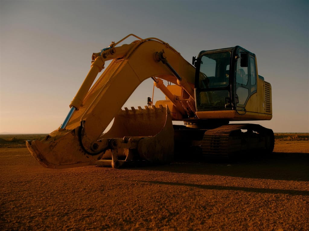 A tracked excavator parked on flat red ground at dusk with its bucket resting down