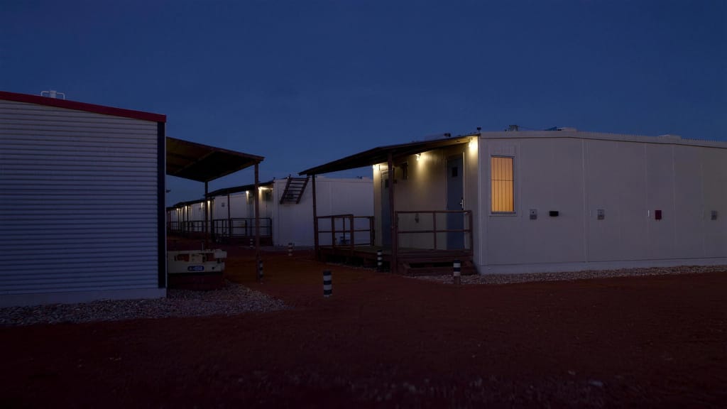 Rows of accommodation units at a work camp at dusk, walkway lights on