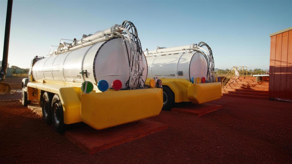 Two water carts parked side by side on red gravel, tanks still clean