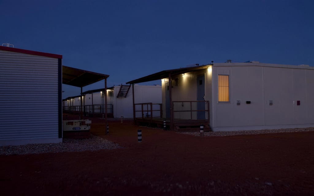 Rows of accommodation units at a work camp at dusk, walkway lights on