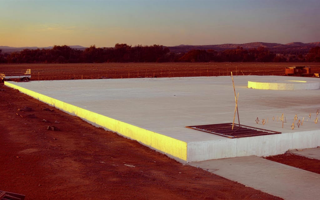 A finished concrete pad at dusk with a round conveyor footing and starter bars set out