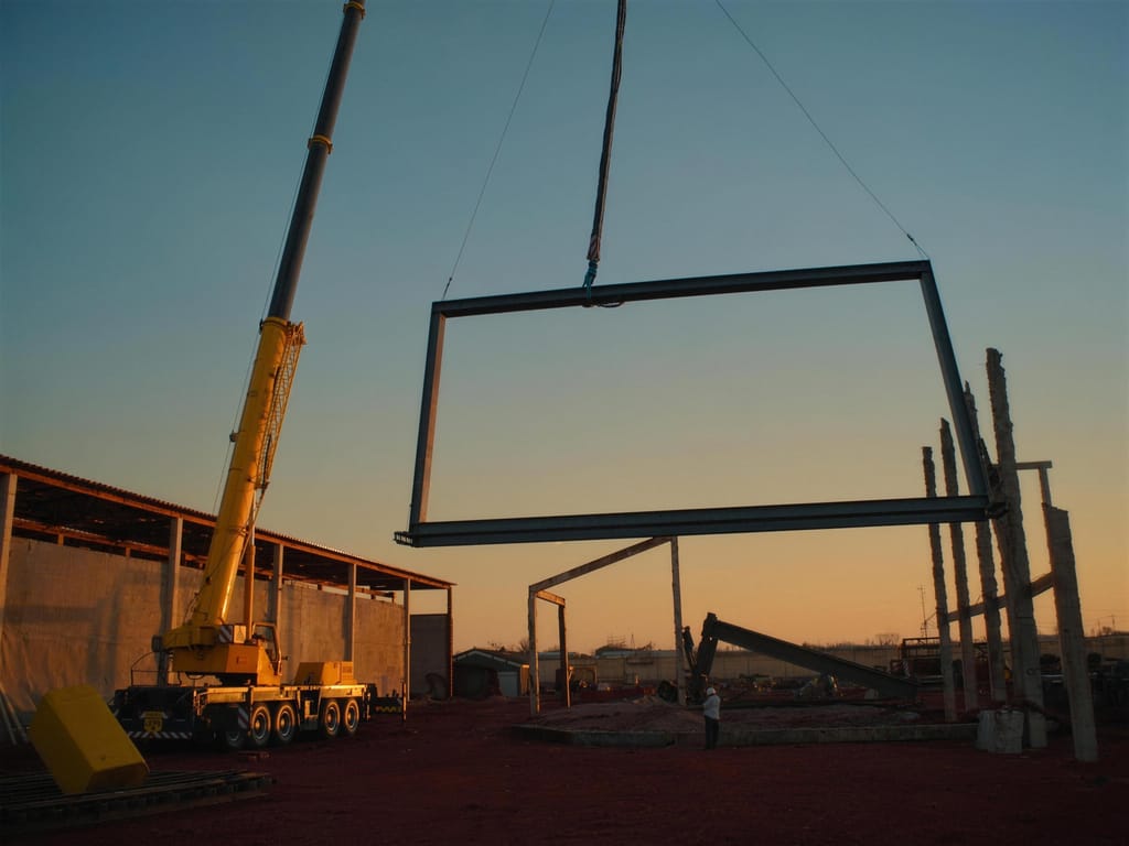A mobile crane holding a large steel frame above a building site at dusk