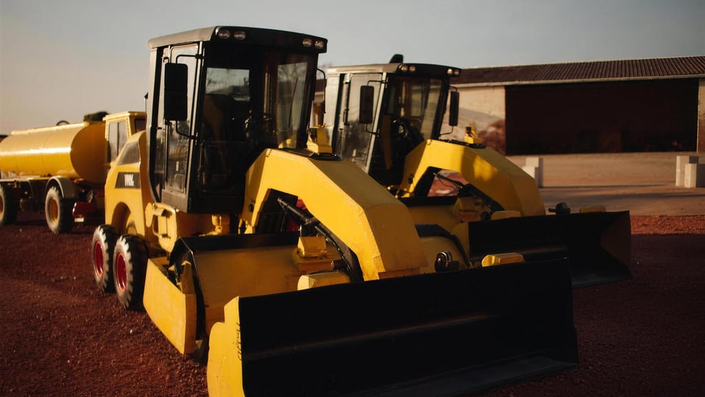 Two graders parked in a row on a red hardstand in late afternoon light