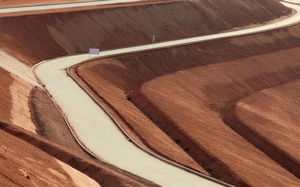 An access track winding between reshaped red embankments, seen from above